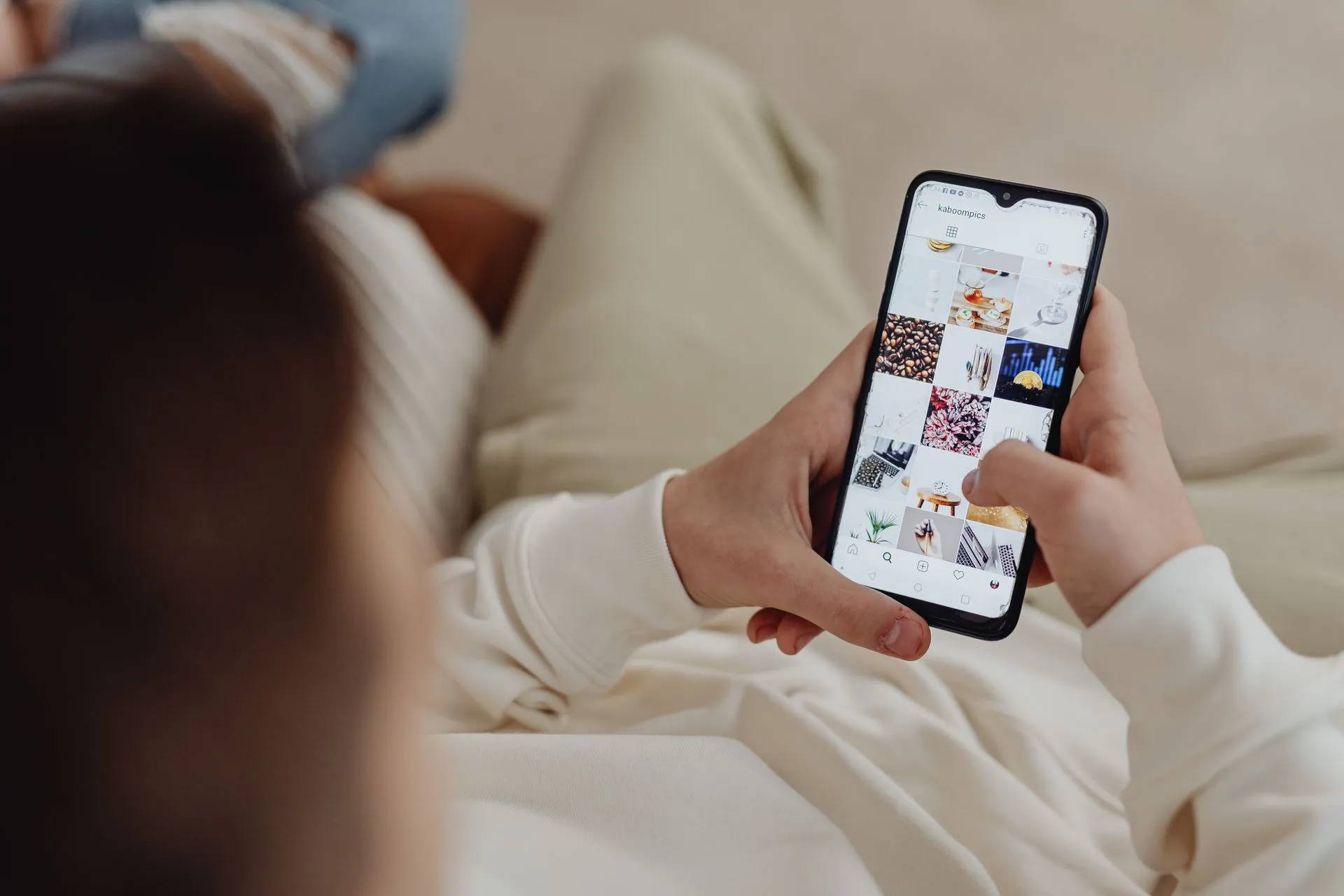 Person on a sofa scrolling a grid of photos on a phone