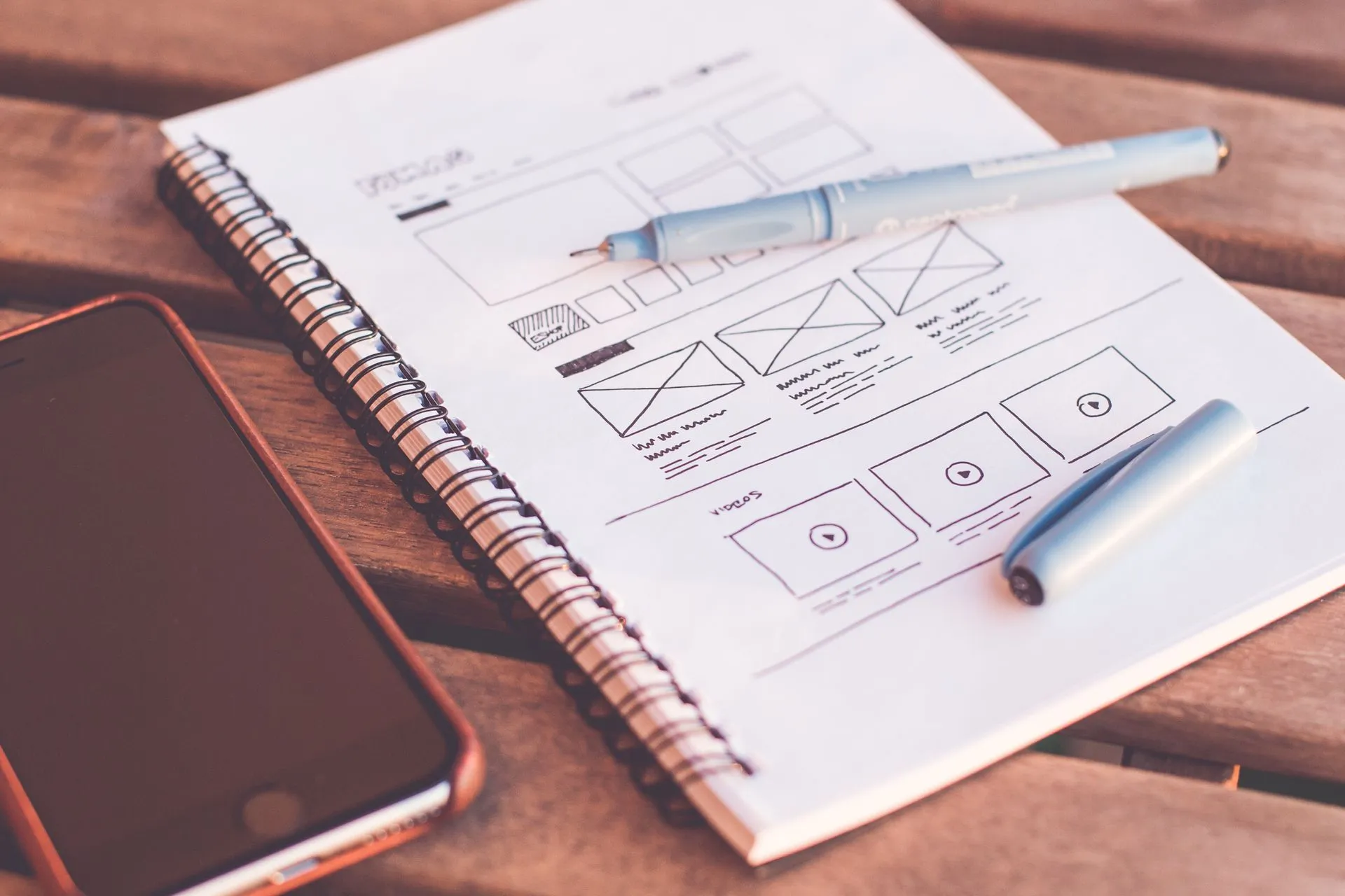 Hand-drawn website wireframes in a notebook next to a phone and a pen